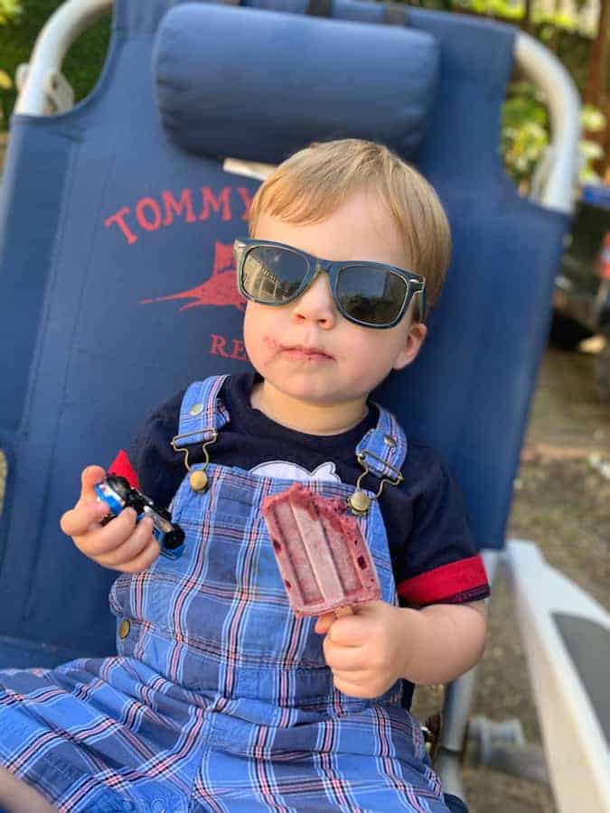 toddler sitting in lawn chair holding matchbox car in one hand and a popsicle in the other