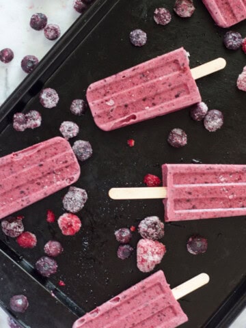 berry popsicles on a baking sheet with frozen berries scattered around