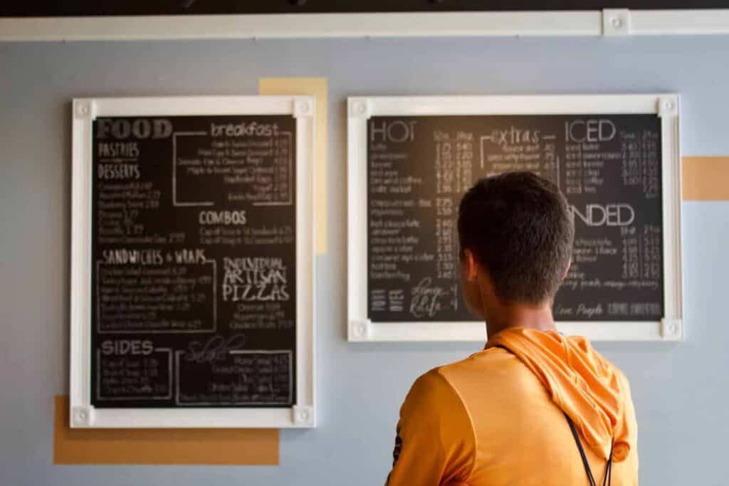 back of person's head standing looking at restaurant menu on wall