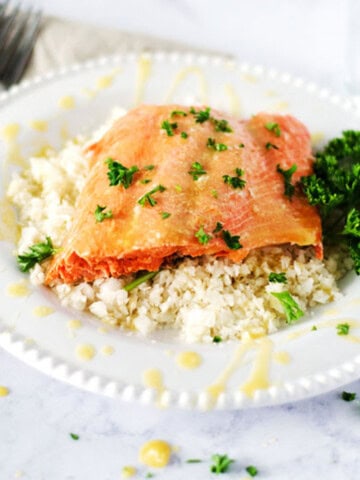citrus glazed salmon on a plate of cauliflower rice topped with fresh parsley