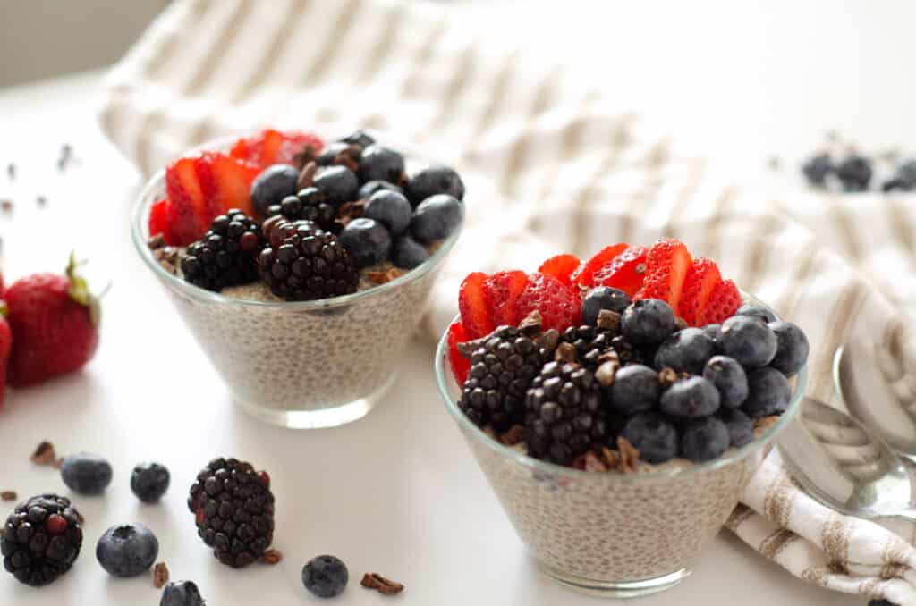 three quarter view of two parfait cups filled with paleo chia seed pudding with almond milk topped with fresh berries and cocoa nibs