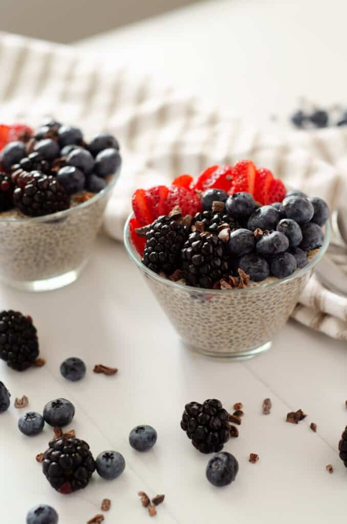 Close up of glass bowl filled with paleo chia seed pudding with almond milk topped with fresh berries and cocoa nibs