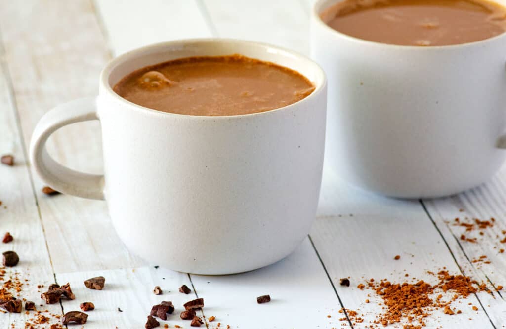 Two white coffee mugs full of homemade vegan hot chocolate on a countertop