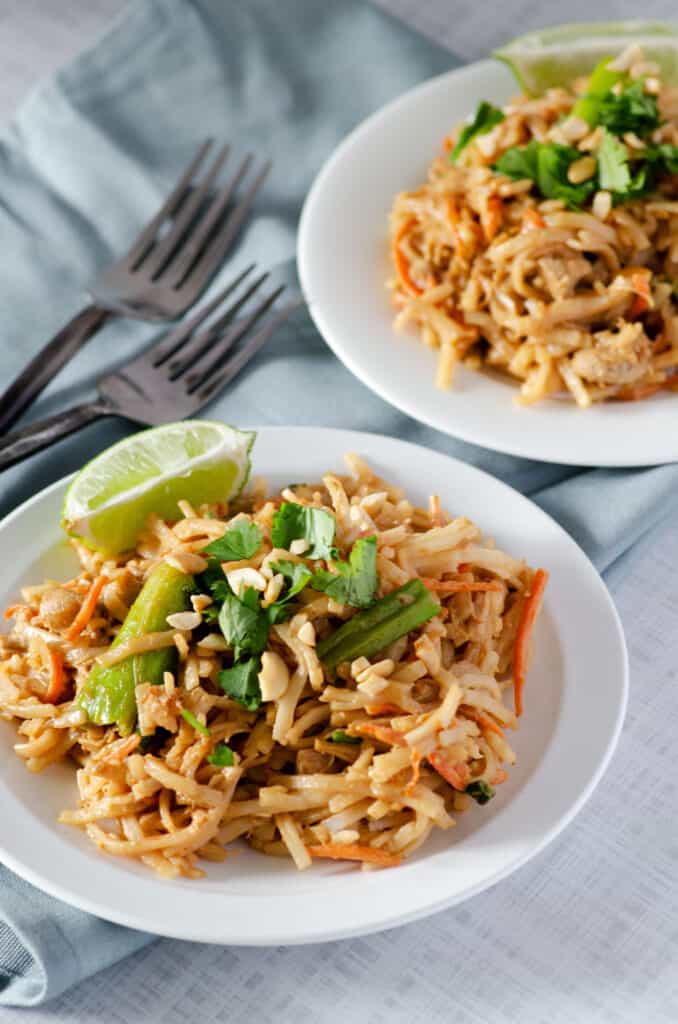 Gluten free pad thai on a plate topped with cilantro and chopped cashews with a slice of lime