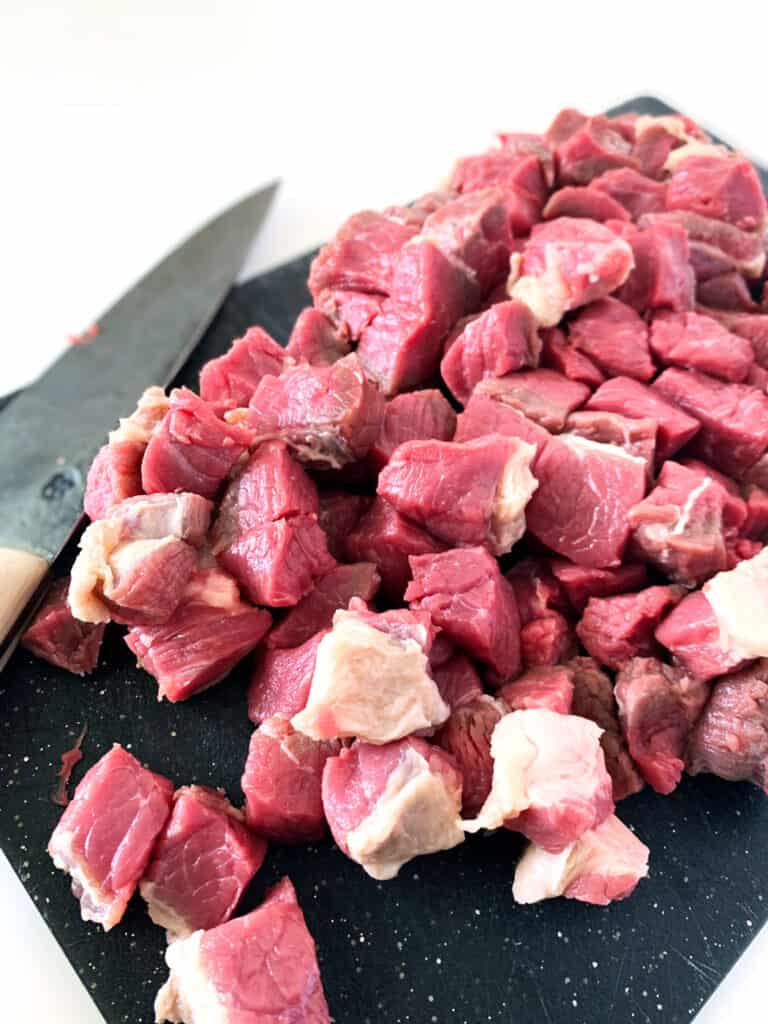 chuck roast cut up into chunks on a cutting board with a knife