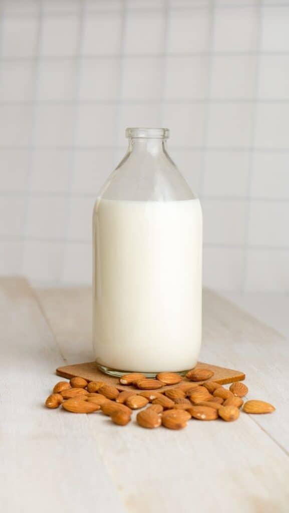 Glass bottle full of almond milk sitting on counter surrounded by almonds