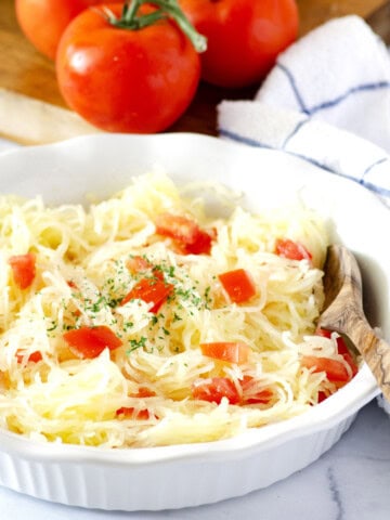 shallow white dish filled with shredded spaghetti squash and diced tomatoes with a wooden serving spoon