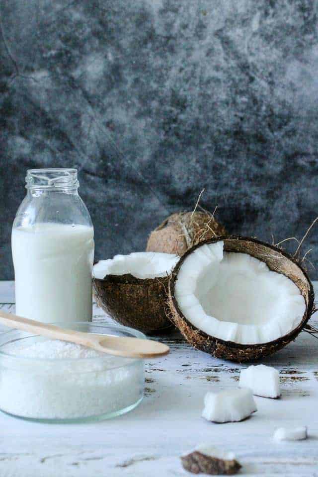 Glass jar of coconut milk surrounded by broken pieces of coconut