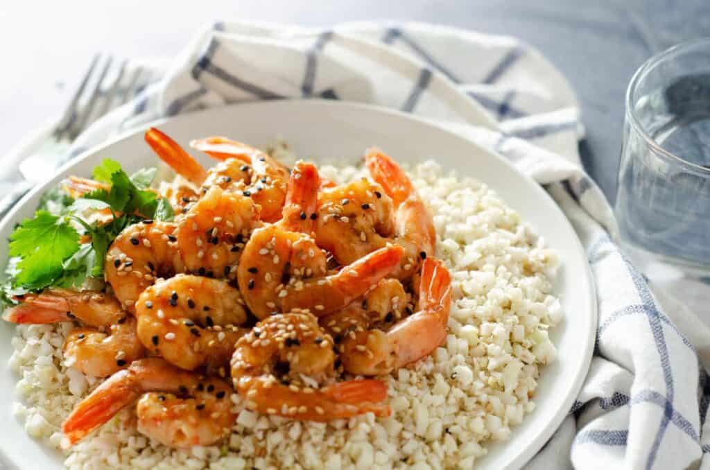 Plate of cauliflower rice topped with whole30 shrimp and sprinkled with sesame seeds