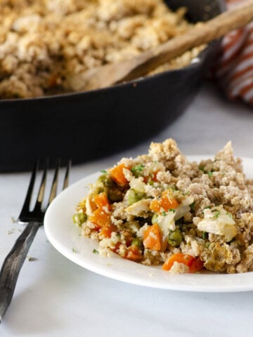grain free chicken pot pie casserole on a plate with a cast iron skillet and serving spoon in the background