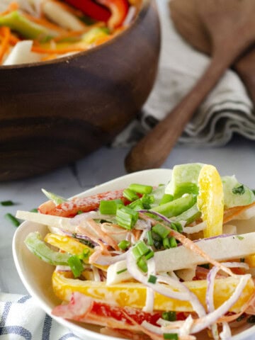 fresh salad of rainbow colored vegetables in a bowl with a large salad bowl in the background