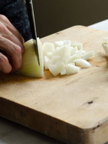 a yellow onion being diced on a cutting board with a pile of cut onions next to it