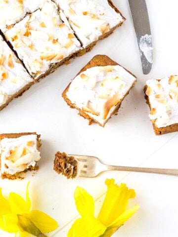 overhead view of squares of carrot cake with frosting cut with a bite on a fork and daffoldils
