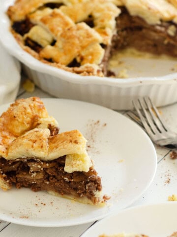 slice of gluten free apple pie on a plate with pan of apple pie in the background