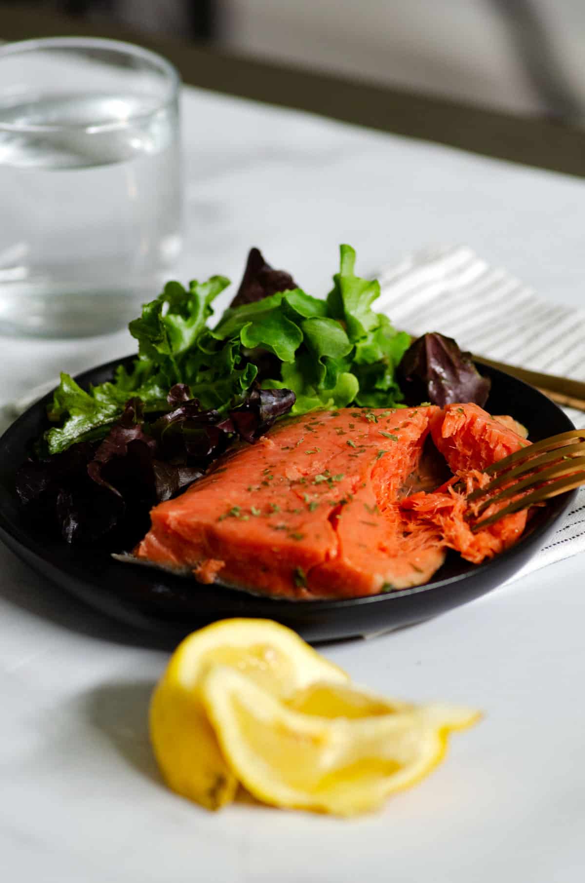 sous vide salmon filet on black plate with lemon wedges being pulled apart by fork