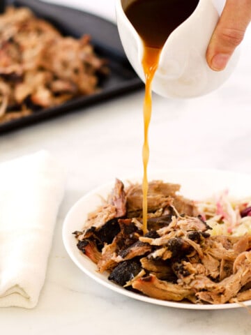 small white pitcher of vinegar bbq sauce being poured over pulled pork