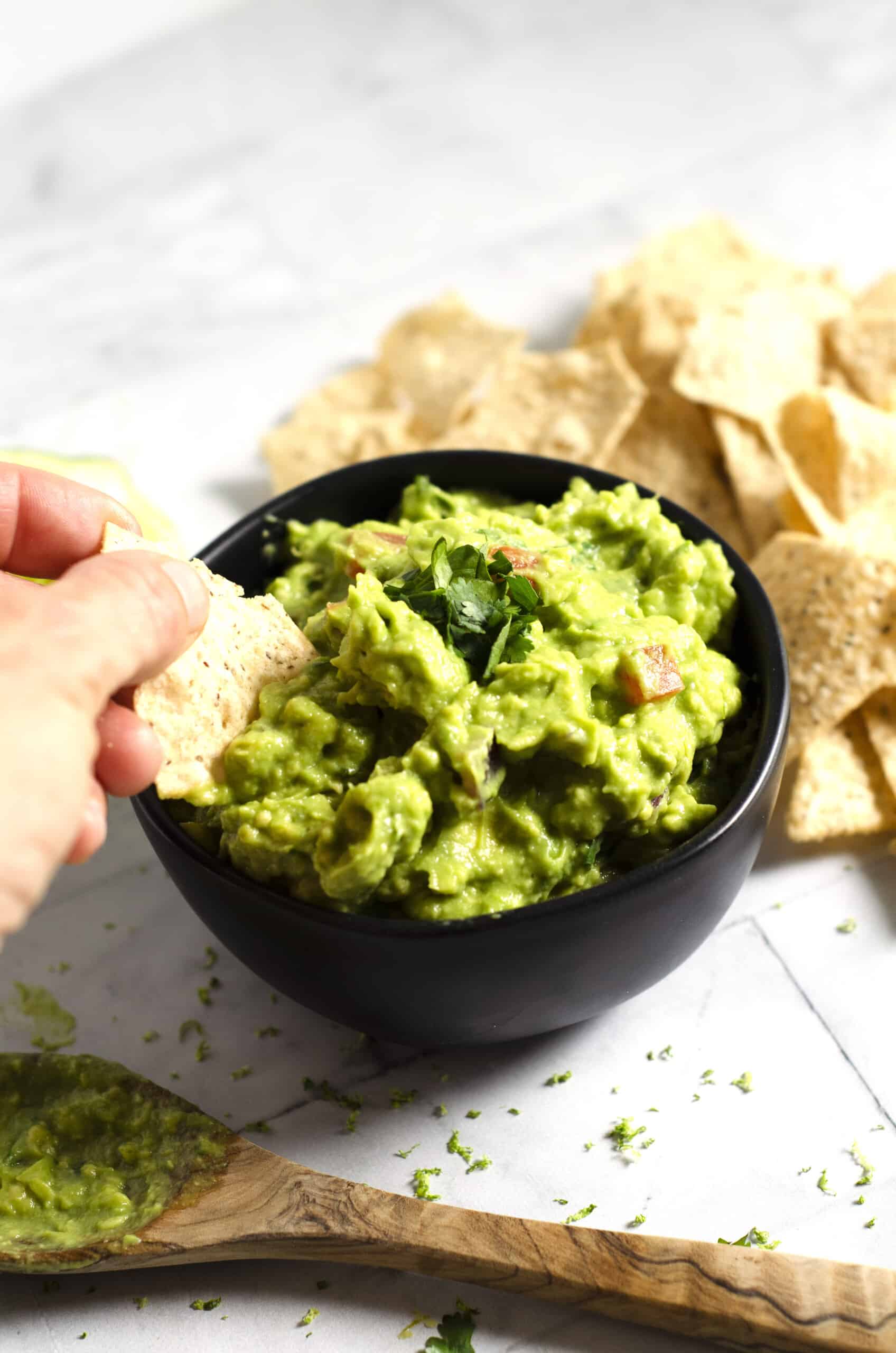 Close up of black bowl full of guacamole with a hand holding a chip and dipping into the bowl