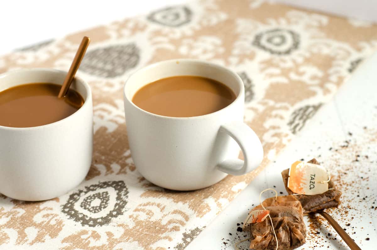 Two white mugs of dirty chai latte with two used tea bags on the counter