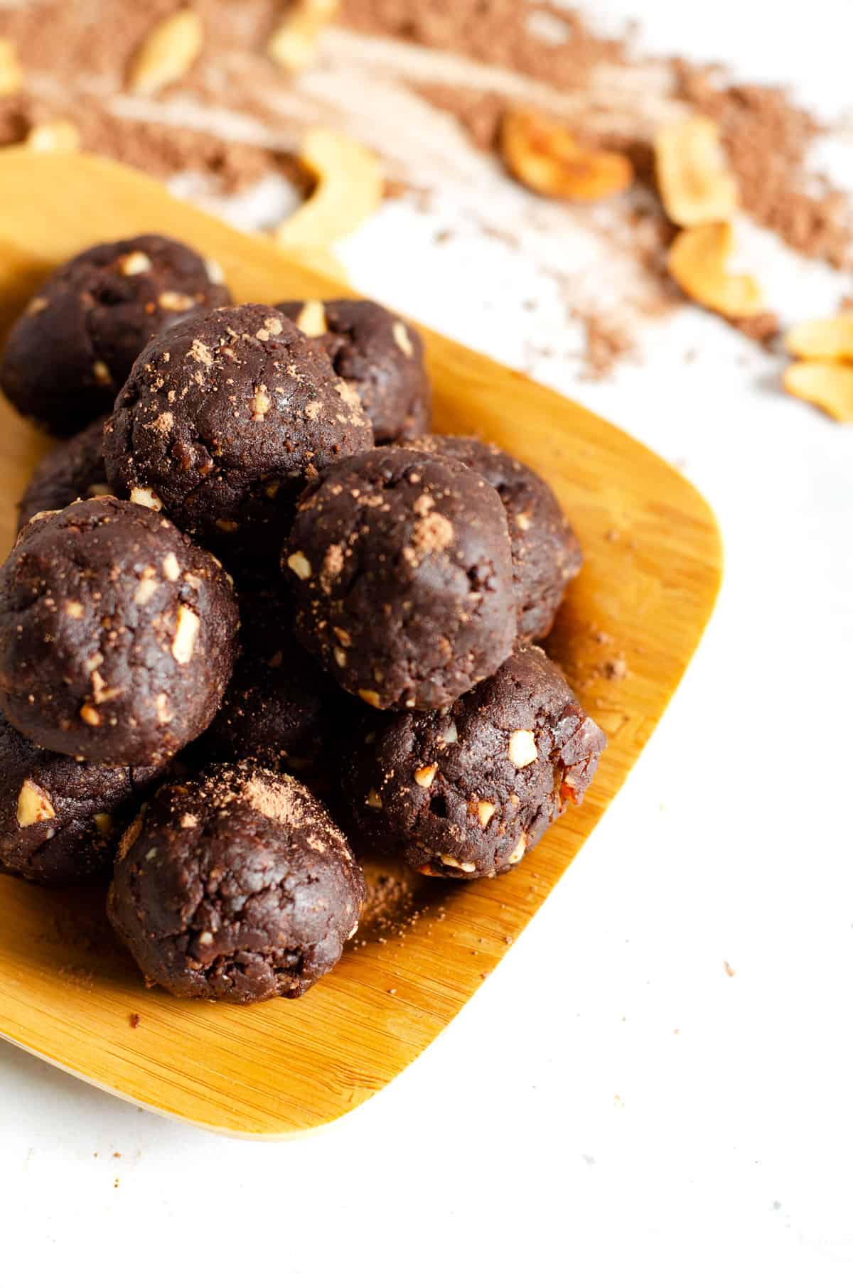 Close up image of chocolate paleo protein balls stacked in a pyramid on a bamboo plate with cocoa powder and cashews in the background