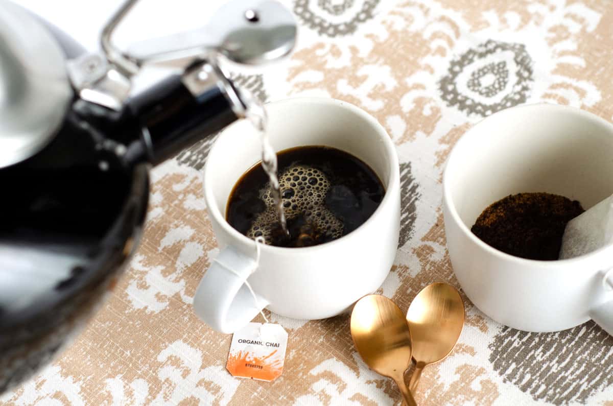 Overhead shot of boiling water being poured into mugs with tea bags in them