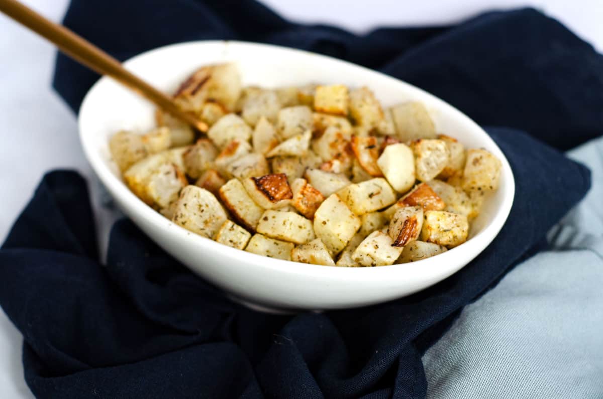 White bowl full of roasted turnip cubes with a gold spoon for serving