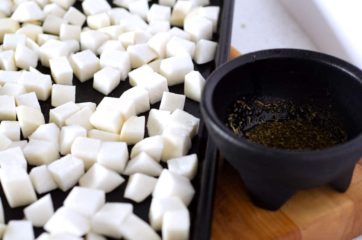 Cubed raw turnips on a baking sheet with bowl of oil and spices next to it