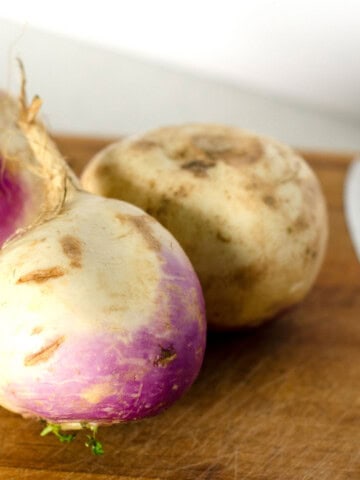 Fresh raw turnips on a wooden cutting board with a chef's knife next to them