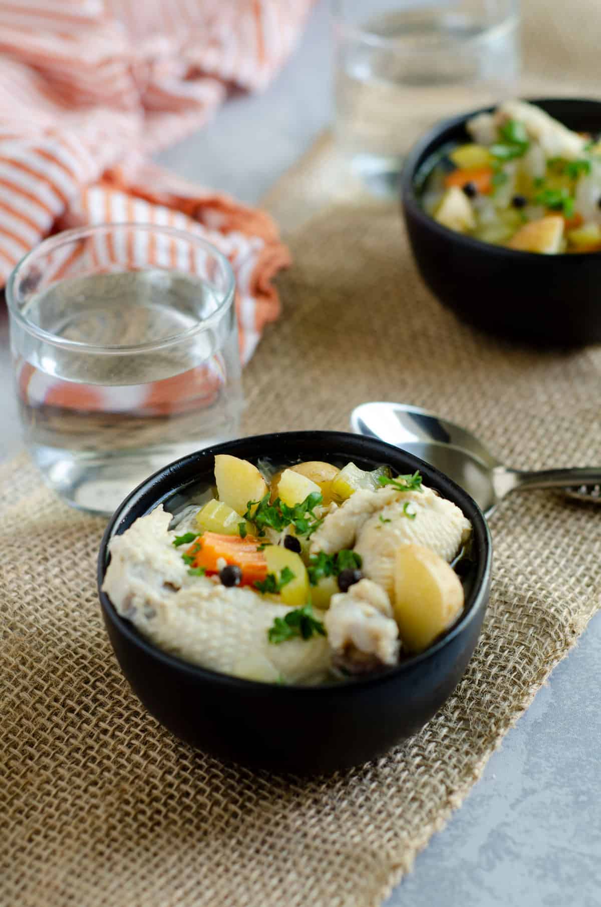 Close up of a bowl of chicken souse with a glass of water in the background