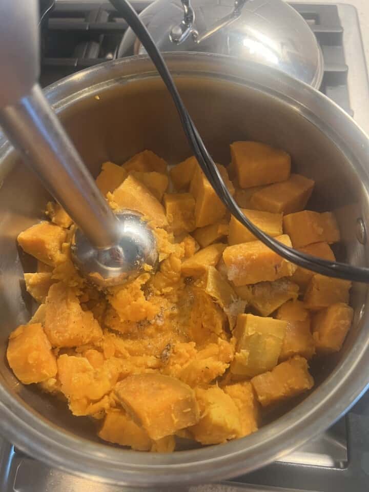 cooked sweet potatoes in pot being blended with immersion blender