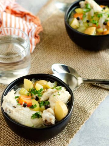 bowls of bahamian chicken souse on a table with spoons and water