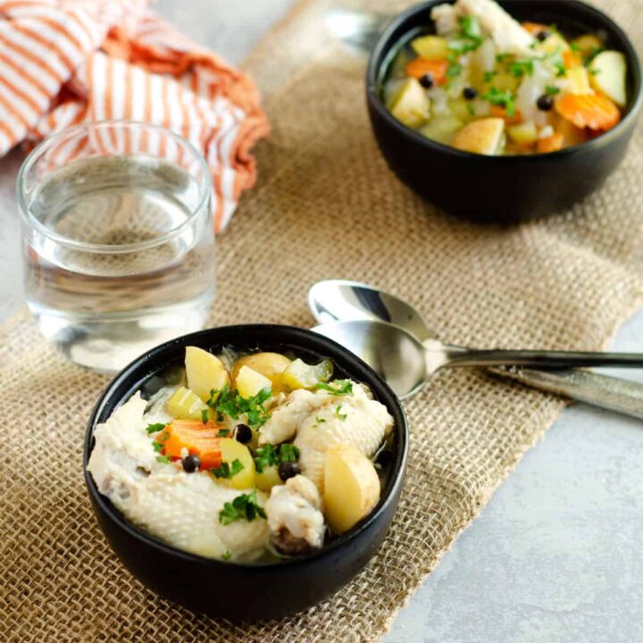 bowls of bahamian chicken souse on a table with spoons and water