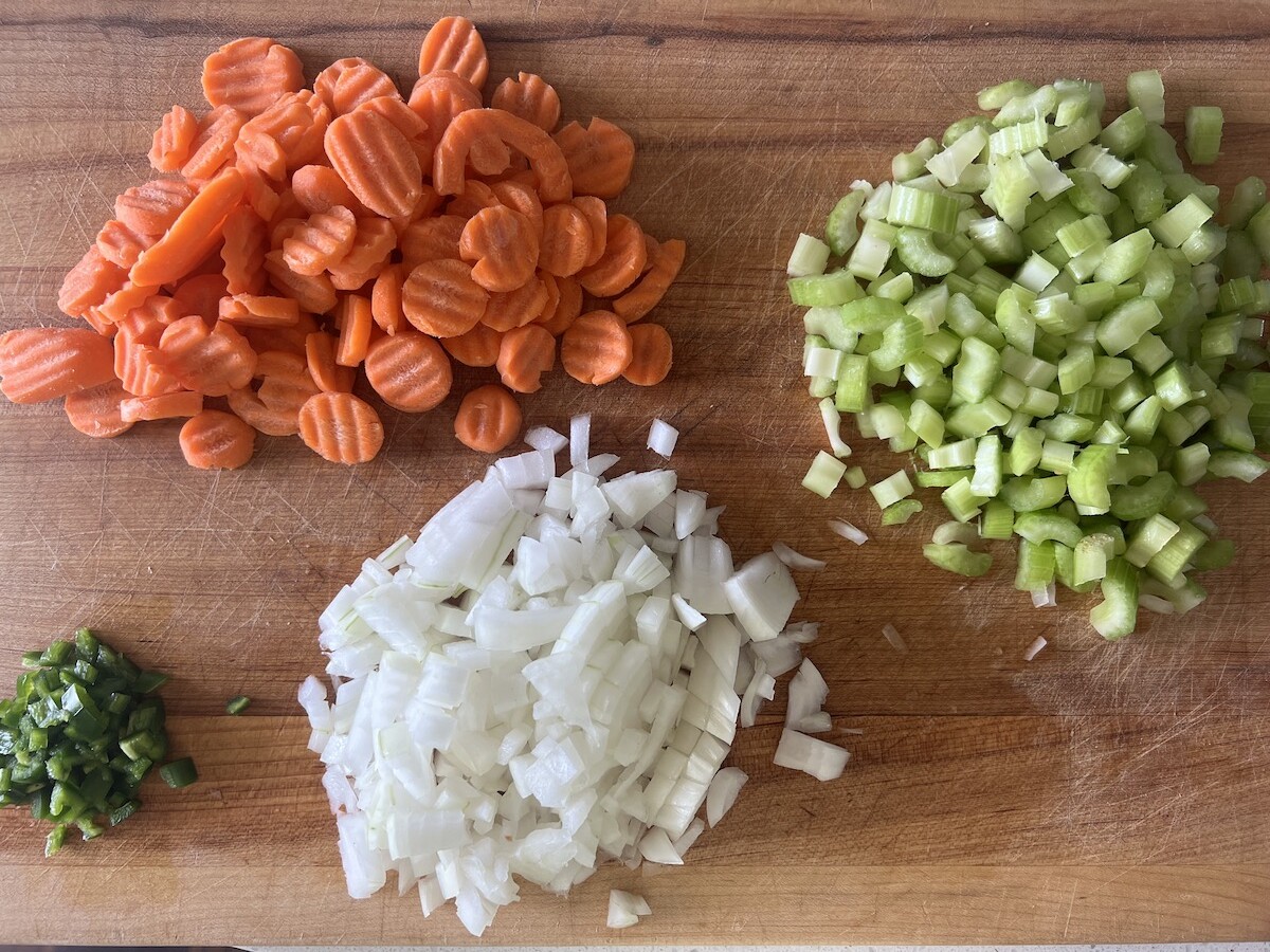 Wooden cutting board with chopped  celery, carrots, onions, and peppers for chicken souse