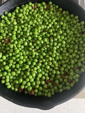 cast iron skillet of shepherd's pie with sweet potato showing middle layer of peas