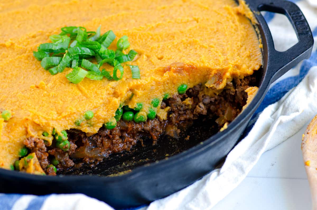 Close up of a cast iron skillet of shepherd's pie with sweet potato with a serving removed showing the layers