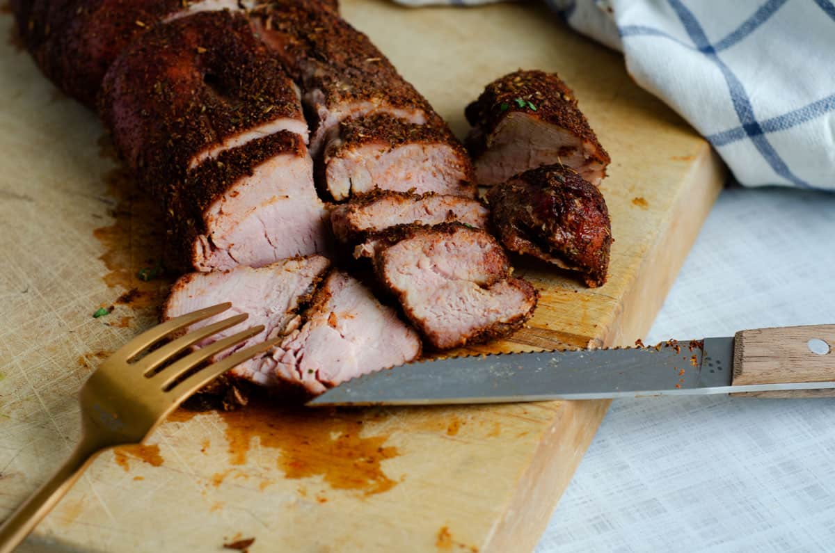 Traeger smoked pork tenderloin sliced on wooden cutting board with knife and fork