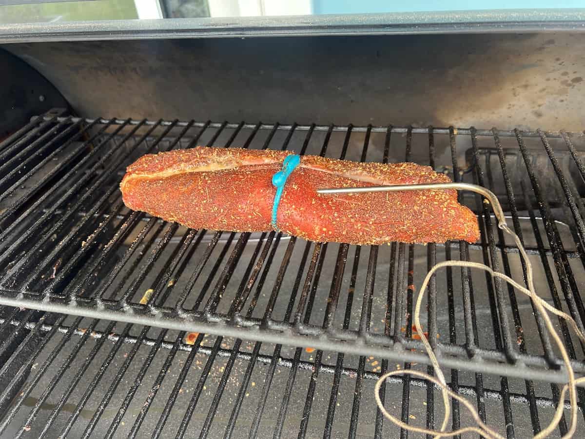 dry rubbed pork tenderloin in pellet grill with meat probe thermometer in it