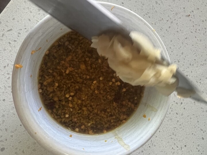 bowl of orange sauce with fresh ginger being added