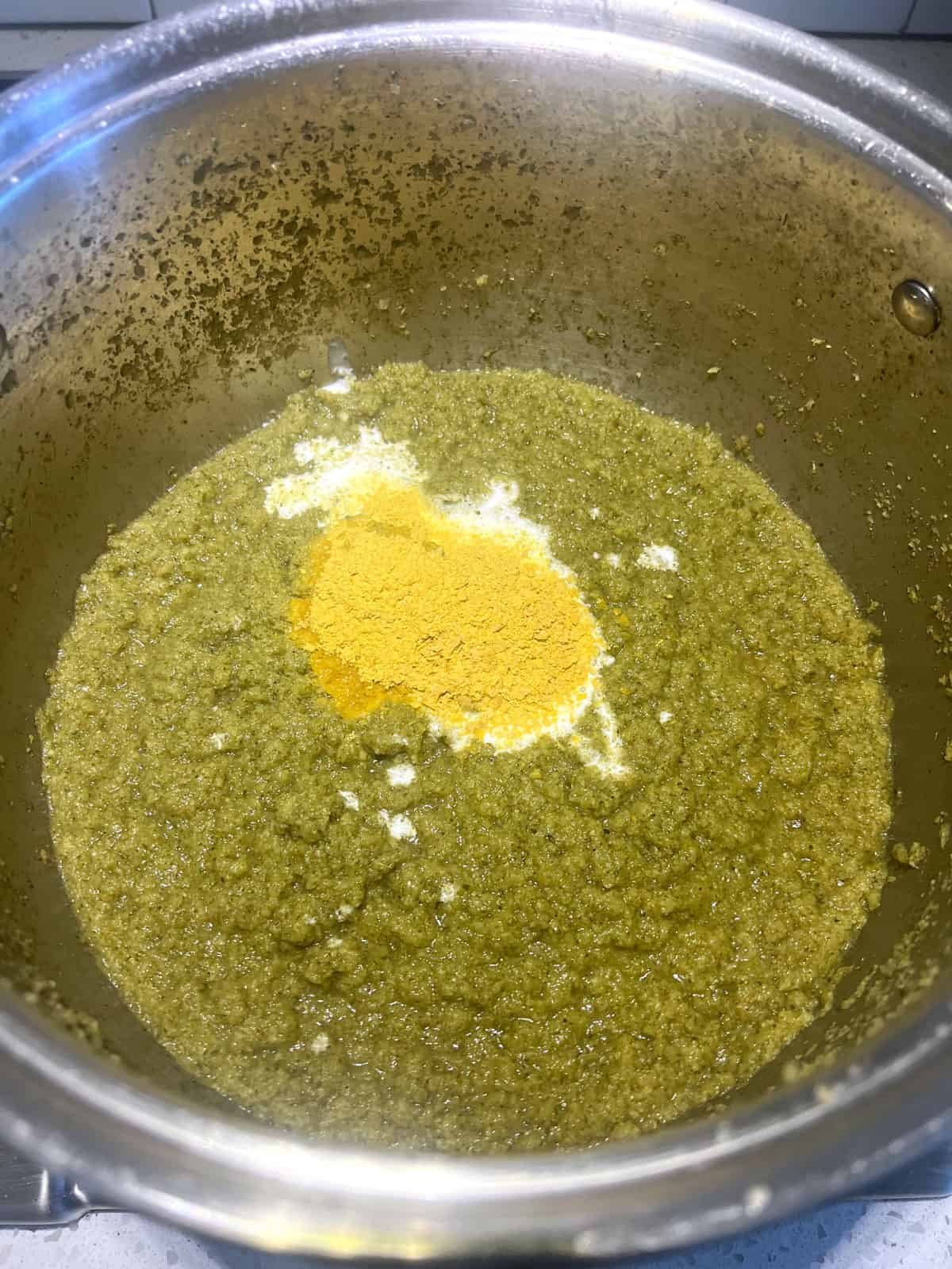 Broccoli soup in pot with coconut milk and nutritional yeast added on top