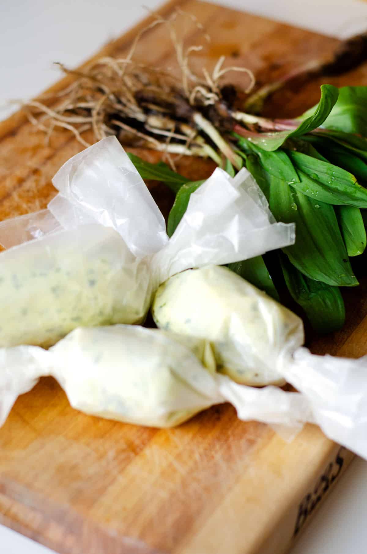 compound ramp butter rolled in wax paper on a wooden cutting board with fresh ramps in the background