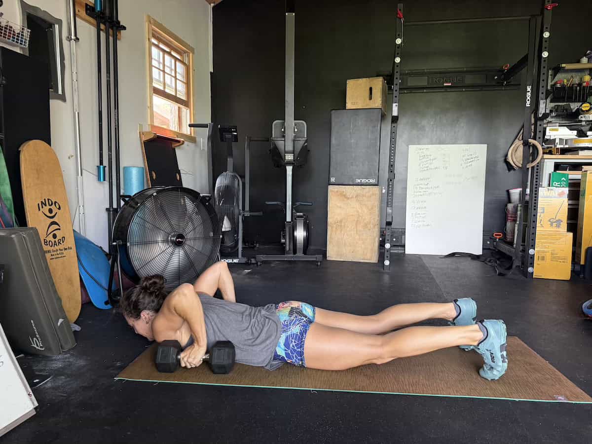 side view of a woman lying in the bottom of a push up in a gym with a dumbbell in each hand