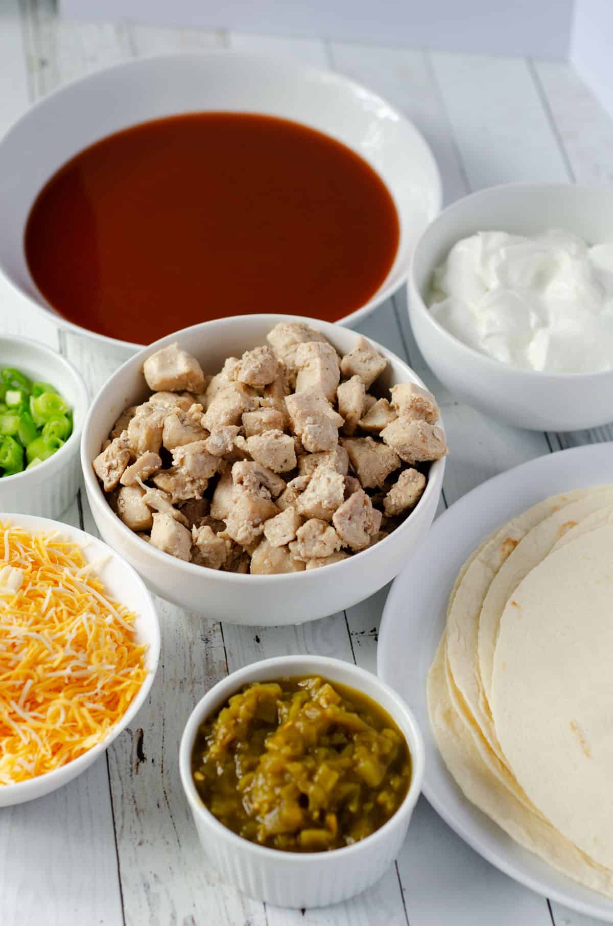 arrangement of white bowls with ingredients in them to make chicken enchiladas