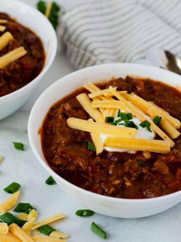 bowl of venison chili topped with sour cream, cheddar cheese, and green onions