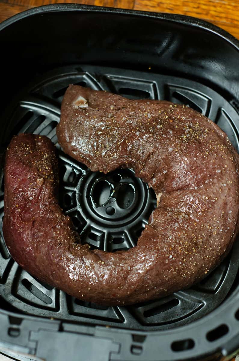 overhead view of a raw venison tenderloin in an air fryer basket before cooking