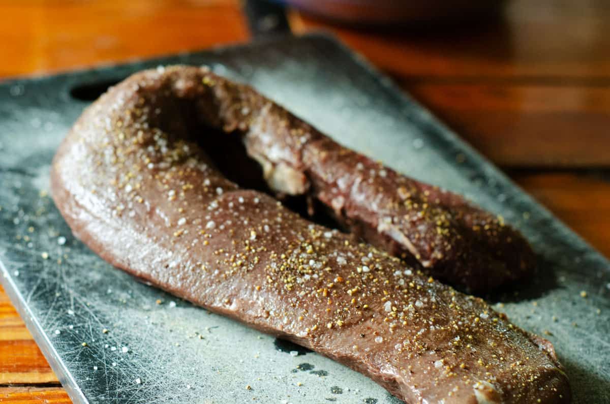 raw venison backstrap on a cutting board, seasoned with dry spices
