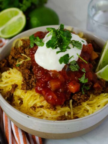 bowl of taco spaghetti squash topped with salsa and sour cream and slices of lime