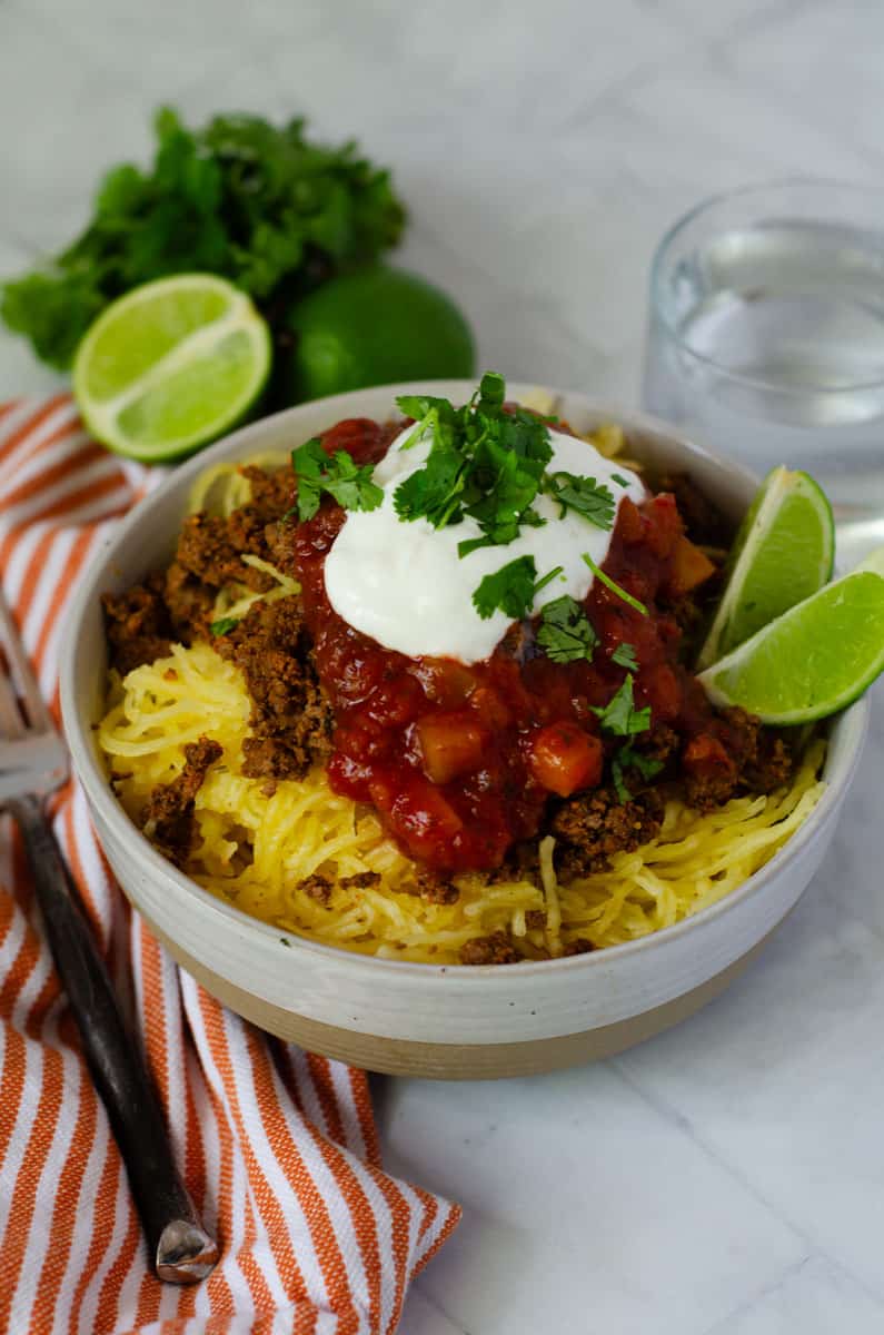bowl of spaghetti squash topped with taco meat, salsa, greek yogurt, cilantro, and served with slices of lime