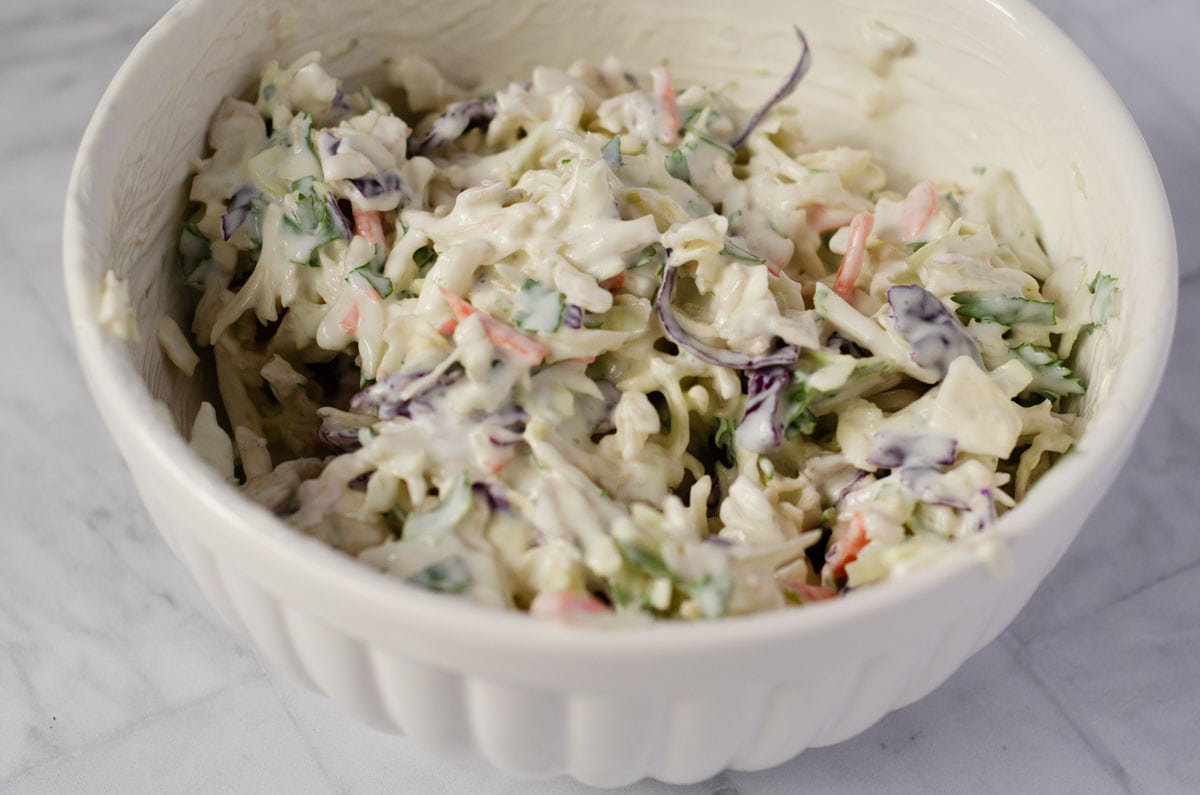 side view of a white serving bowl filled with a creamy coleslaw