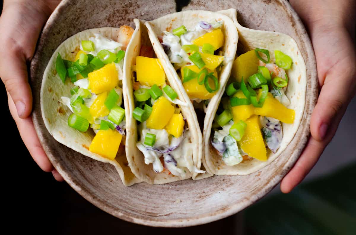 an overhead image of a bowl of shrimp tacos held by two hands on the sides 