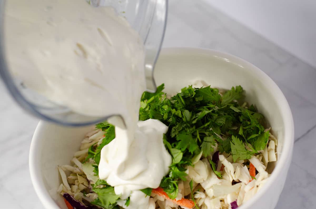 bowl of coleslaw mix getting sauce poured onto it from a blender