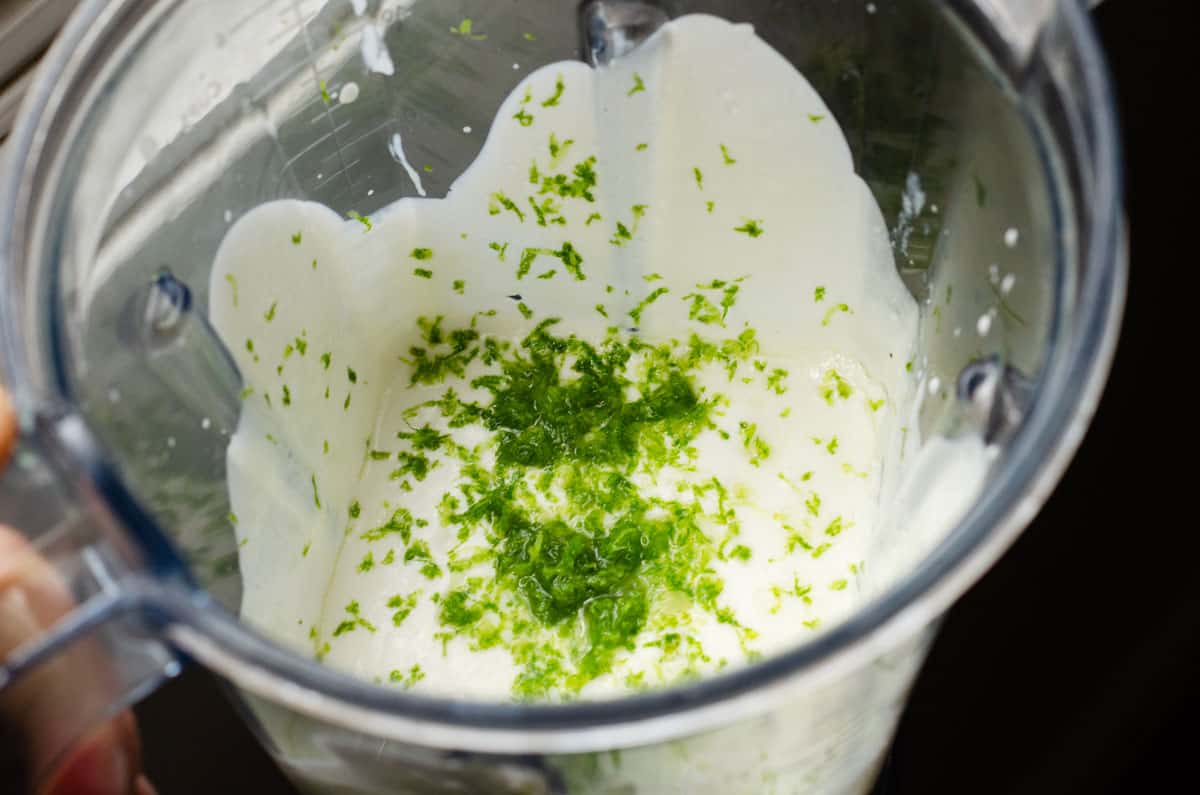 overhead view of a blender with a creamy sauce in it with lime zest on top